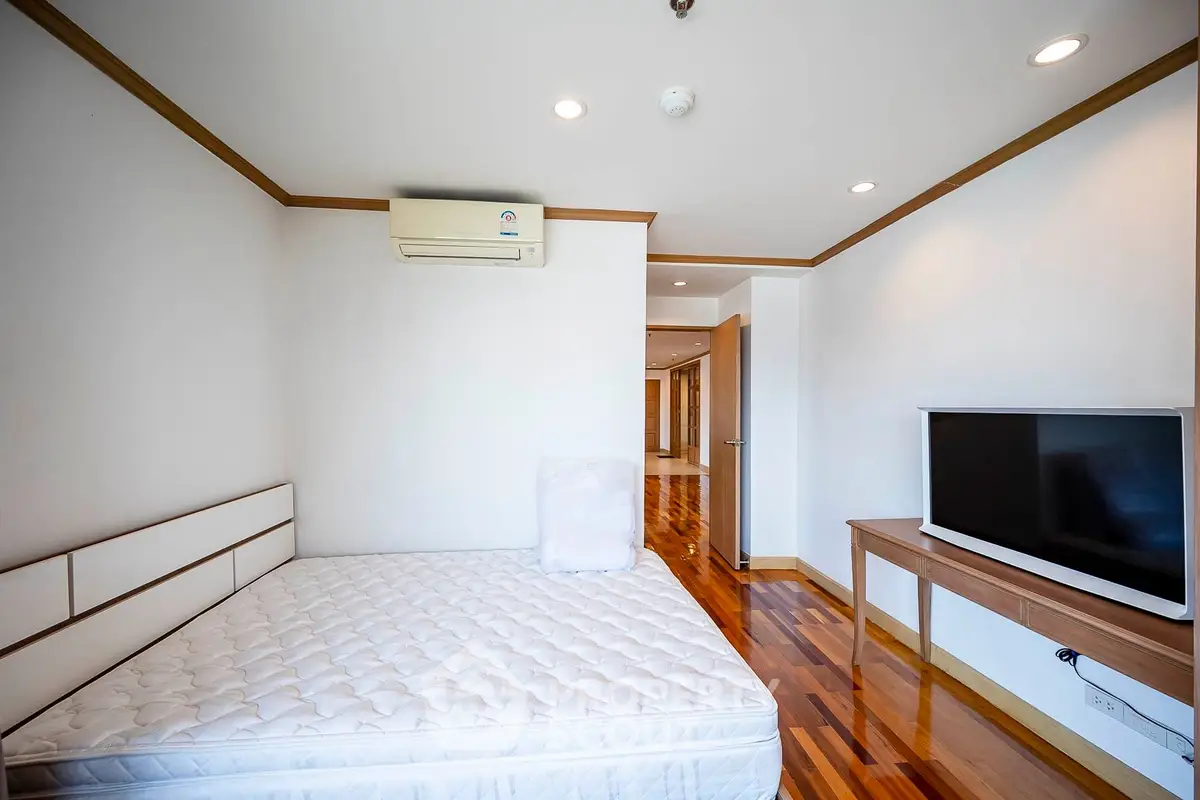 Spacious bedroom with modern decor and hardwood floors, featuring a large bed and flat-screen TV.