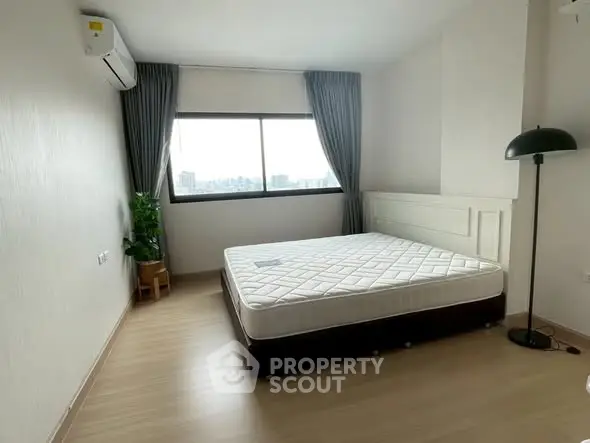 Spacious bedroom with large window and modern decor in a high-rise apartment.