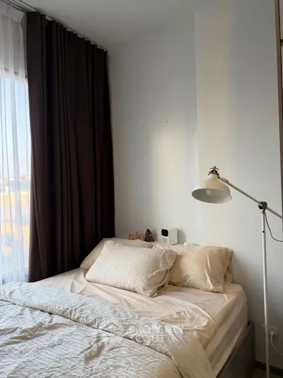 Cozy bedroom with natural light and modern decor, featuring a comfortable bed and stylish lamp.