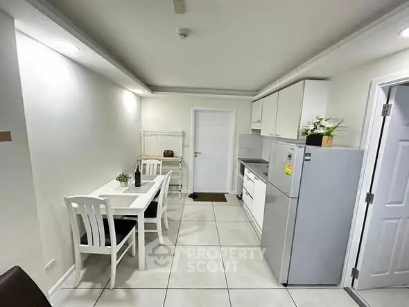 Modern kitchen with dining area, sleek white cabinets, and stainless steel fridge.