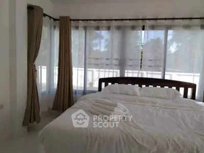 Spacious bedroom with large windows and elegant curtains, offering a serene and airy ambiance.