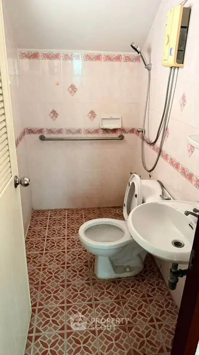 Compact bathroom with tiled floor, shower, and toilet in cozy real estate unit.