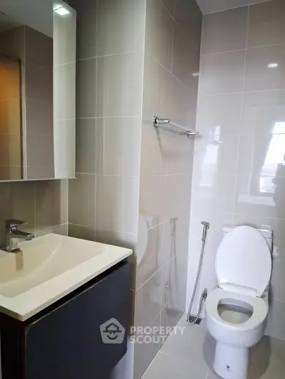 Modern bathroom with sleek fixtures and neutral tiles, featuring a toilet and a stylish sink.