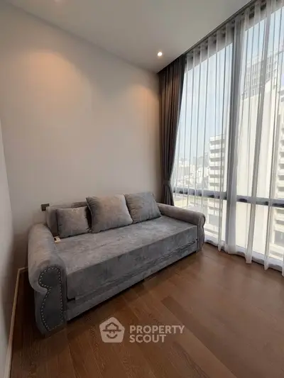 Stylish living room with elegant gray sofa and floor-to-ceiling windows offering city views.