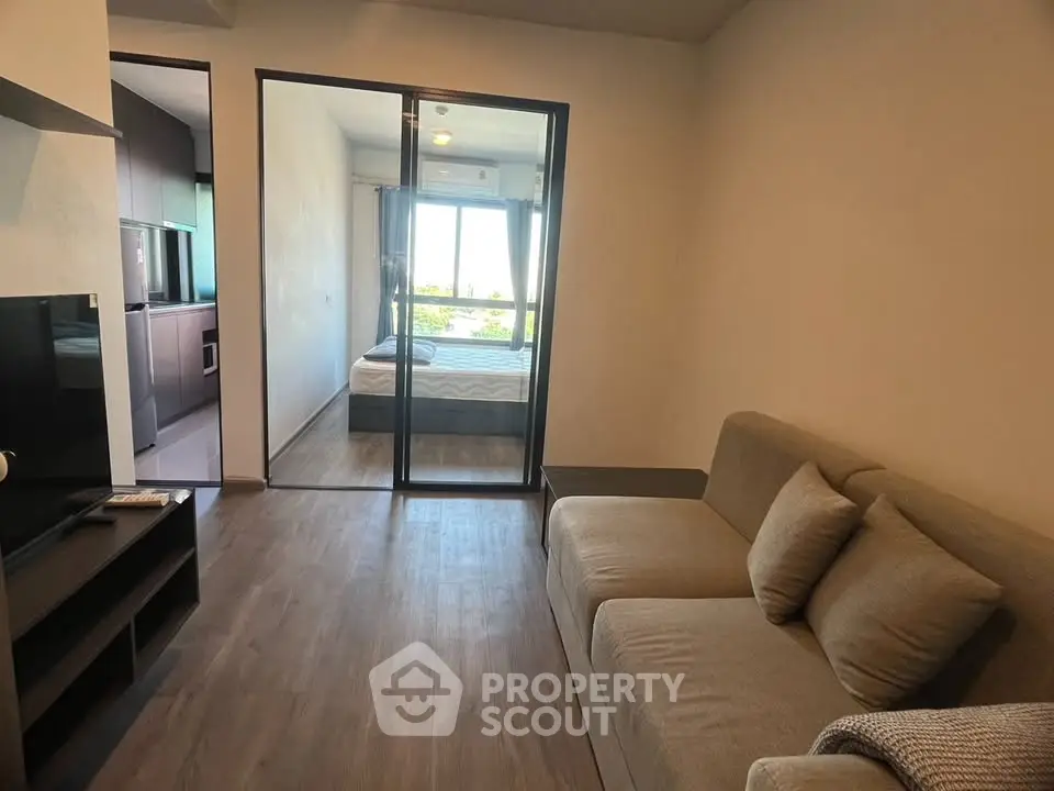 Modern apartment living room with cozy sofa and glass partition leading to bedroom.
