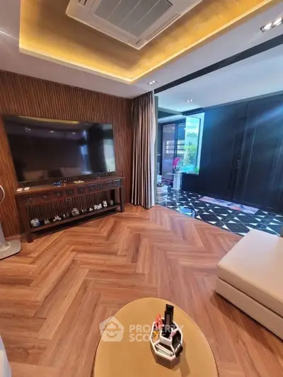Luxurious living room with modern decor and large TV, featuring elegant herringbone flooring.