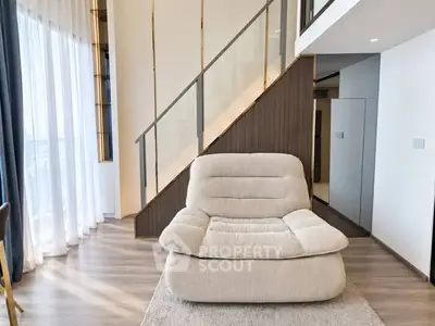Modern living room with stylish staircase and cozy armchair, featuring elegant design and natural light.