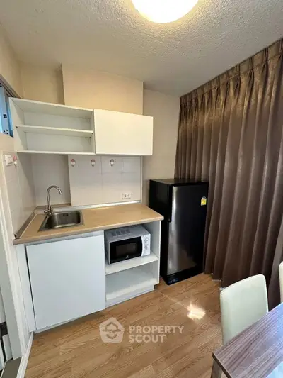 Compact kitchen with modern appliances and wooden flooring in cozy apartment.