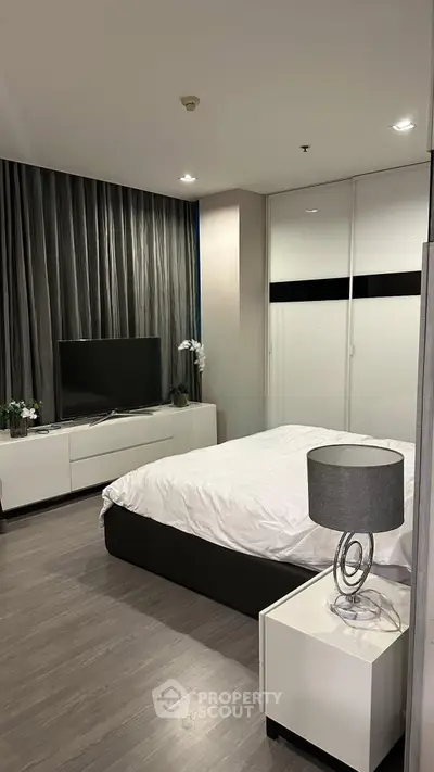 Modern bedroom with sleek design, featuring a cozy bed, stylish lamp, and flat-screen TV for ultimate comfort.