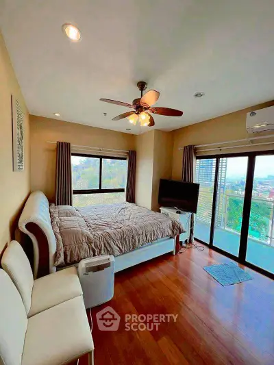 Spacious bedroom with large windows and city view, featuring modern furniture and wooden flooring.