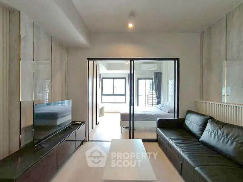 Modern living room with sleek black sofa and glass partition leading to bedroom.
