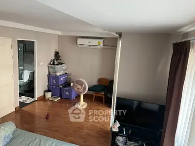 Cozy living room with wooden flooring and air conditioning, featuring a TV and a glimpse into the bathroom.