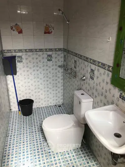 Compact bathroom with tiled walls and floor, featuring a toilet, sink, and shower area.