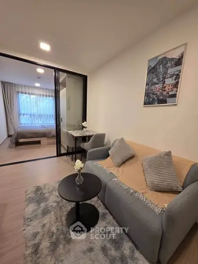 Modern living room with cozy sofa and view into stylish bedroom through glass partition.