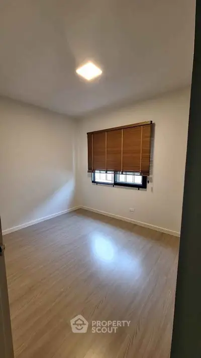 Spacious empty bedroom with wooden flooring and window blinds, perfect for customization.