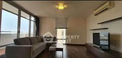 Spacious living room with modern sofa and TV, featuring large windows and balcony access.