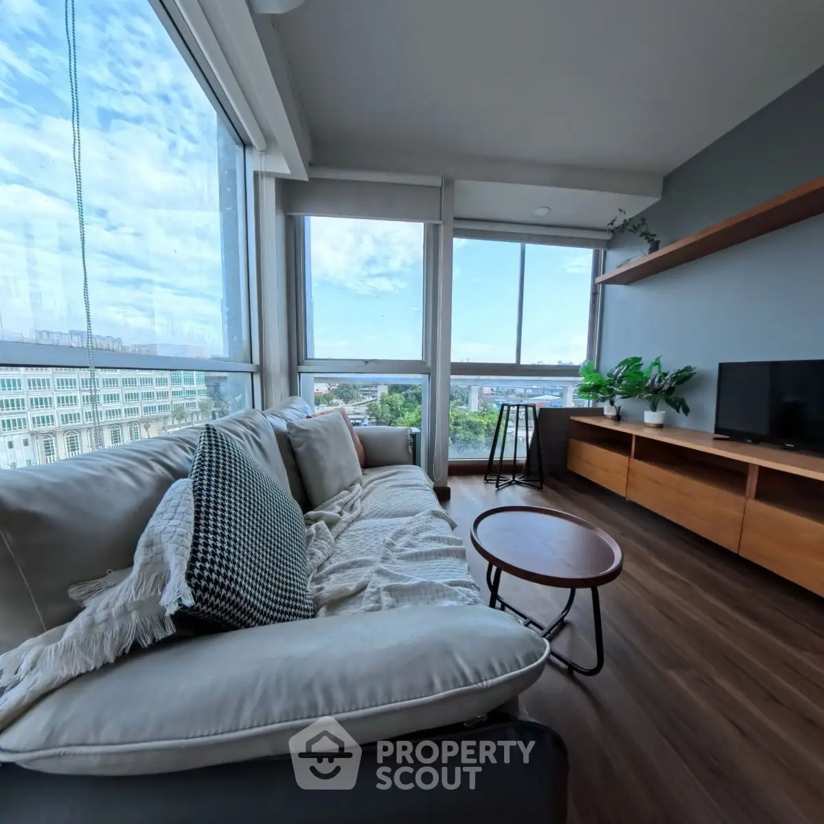 Modern living room with large windows and city view, featuring cozy sofa and stylish decor.