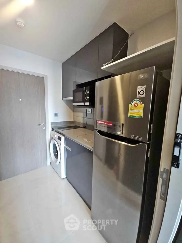 Modern kitchen with sleek appliances and compact design, featuring a washing machine and stainless steel fridge.
