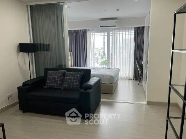 Modern open-plan living room with cozy sofa and bedroom view, featuring floor-to-ceiling windows.