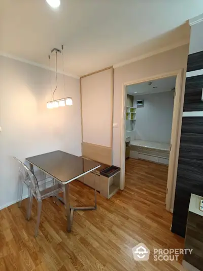 Modern dining area with sleek table and chairs, leading to cozy bedroom with wooden flooring.