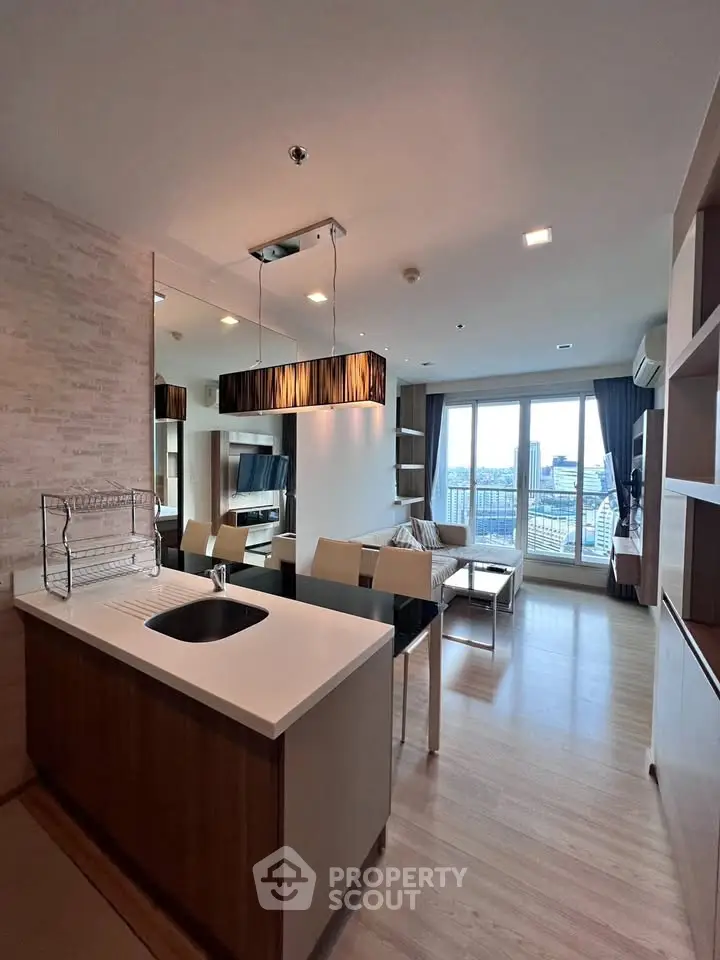 Modern open-layout living room with kitchen, featuring large windows and stylish lighting.