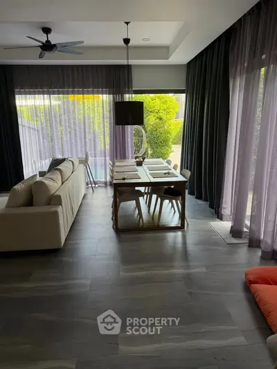 Modern living room with large windows and garden view, featuring stylish furniture and elegant decor.