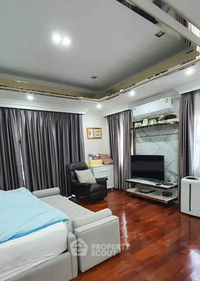 Spacious living room with modern decor and wooden flooring, featuring a cozy seating area and entertainment setup.
