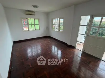 Spacious empty room with wooden flooring and large windows offering natural light.