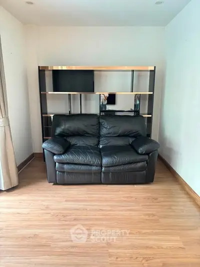 Spacious living room with elegant black leather sofa and modern shelving unit on wooden flooring.
