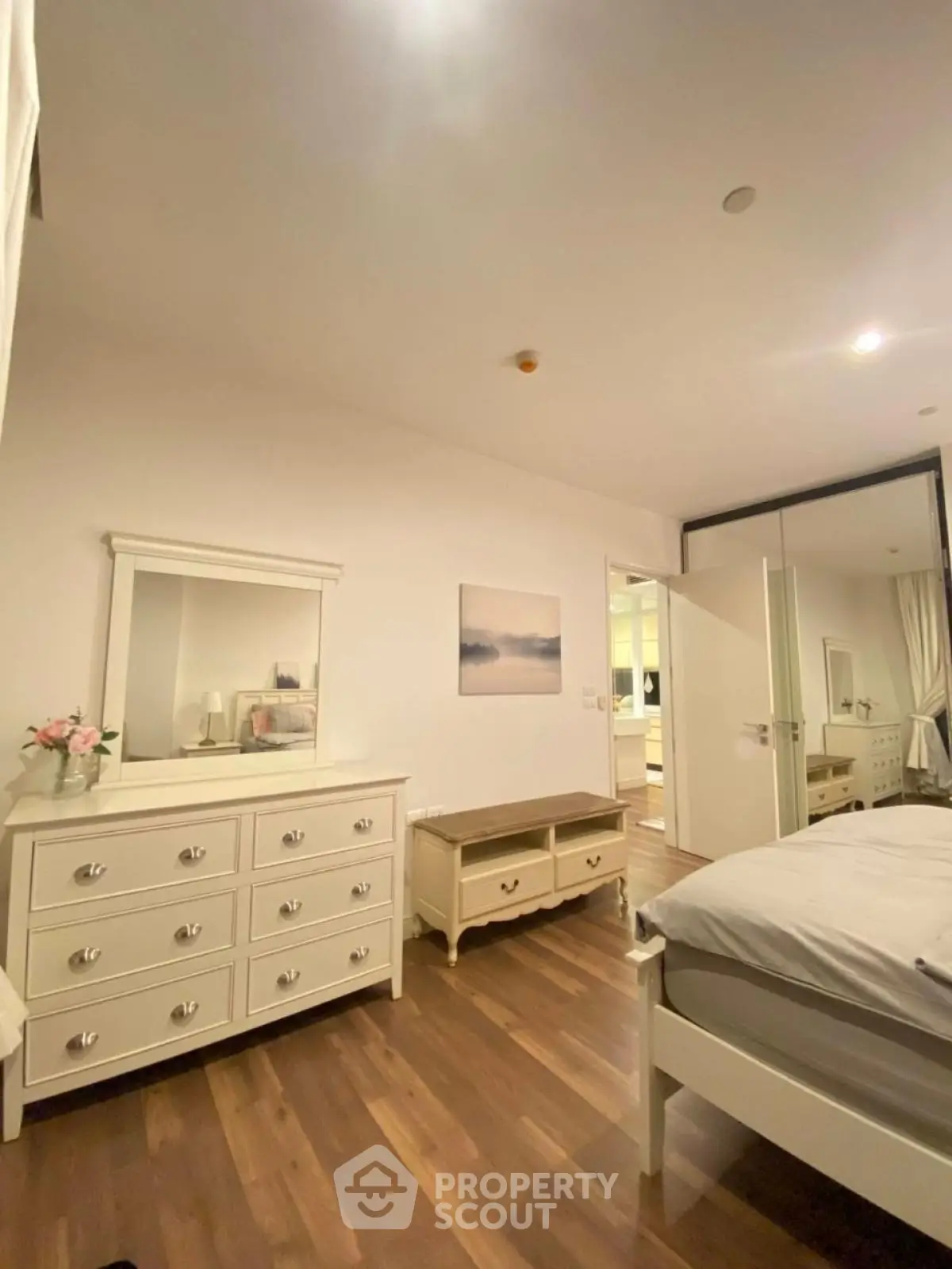 Spacious bedroom with elegant white furniture and wooden flooring, perfect for a cozy and stylish living space.