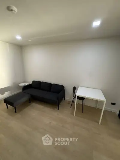 Minimalist living room with black sofa, white table, and wooden flooring.