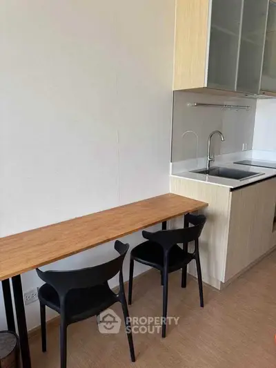 Modern kitchen with sleek design and compact dining area, featuring wooden cabinetry and contemporary chairs.