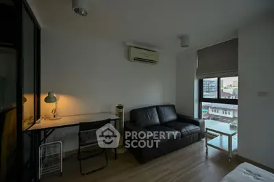 Modern living room with sleek black sofa, work desk, and city view window in a cozy apartment.