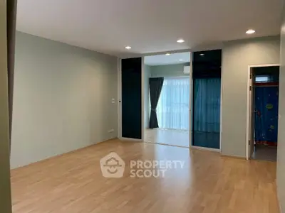 Spacious modern living room with wooden flooring and sliding glass doors leading to a bright balcony.