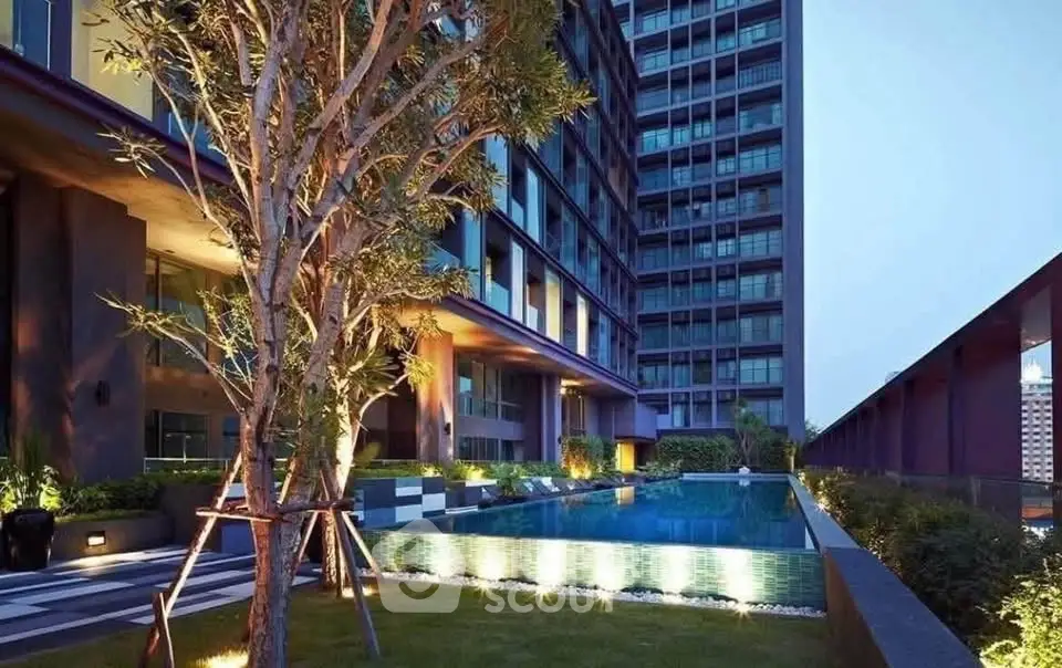 Luxurious modern building with illuminated pool and lush garden area at dusk.