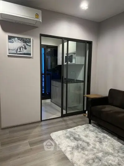 Modern living room with sleek design, featuring a cozy sofa, stylish rug, and a view into a contemporary kitchen.