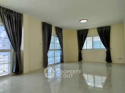 Spacious sunlit living room with large windows and elegant curtains.