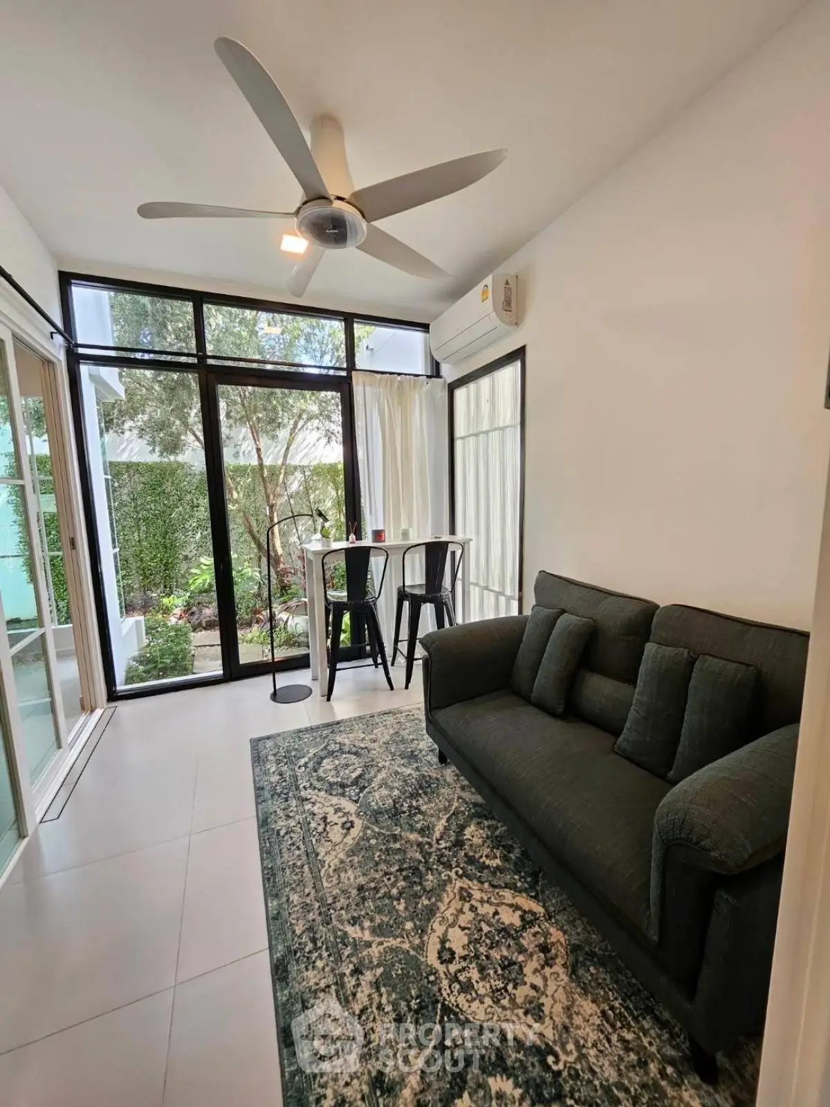 Chic living room with garden view, modern ceiling fan, and cozy seating area in stylish apartment.