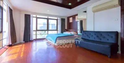 Spacious bedroom with large windows and city view, featuring modern furnishings and wooden flooring.