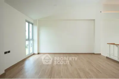 Spacious empty room with wooden flooring and large window, perfect for customization.