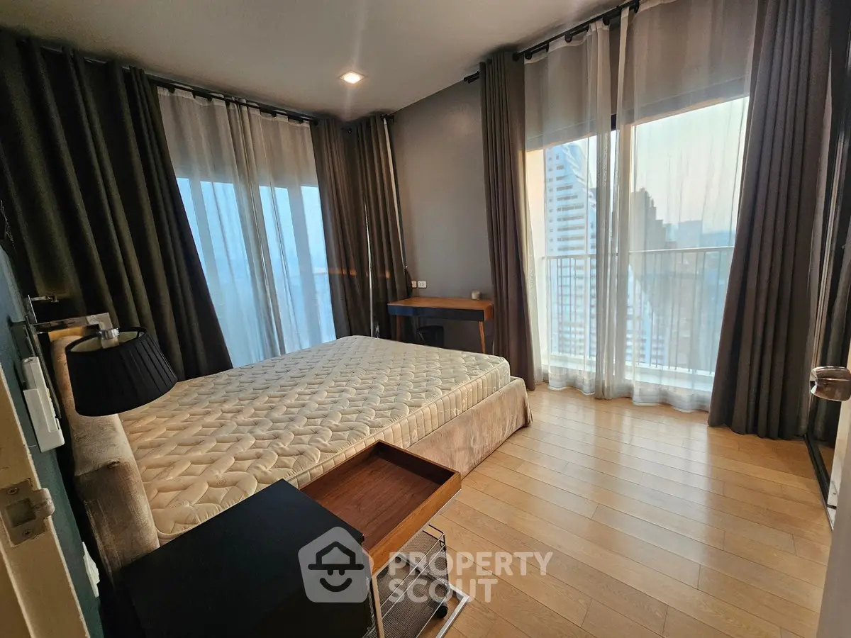 Spacious bedroom with large windows and modern decor in high-rise apartment.