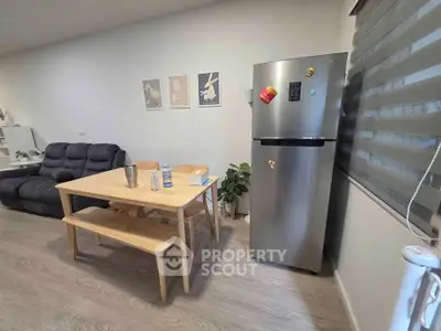 Modern living room with cozy sofa, dining table, and sleek fridge in a bright open space.
