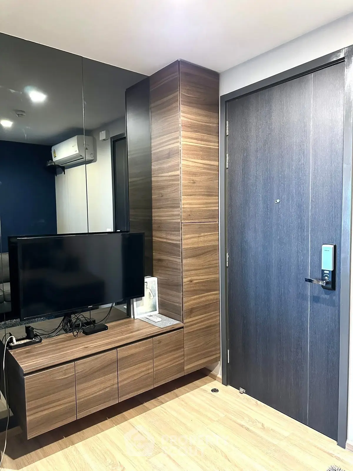 Modern living room with sleek wooden furniture and wall-mounted TV, featuring a stylish entrance door.
