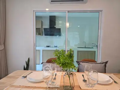 Modern dining area with view into sleek kitchen through glass doors.