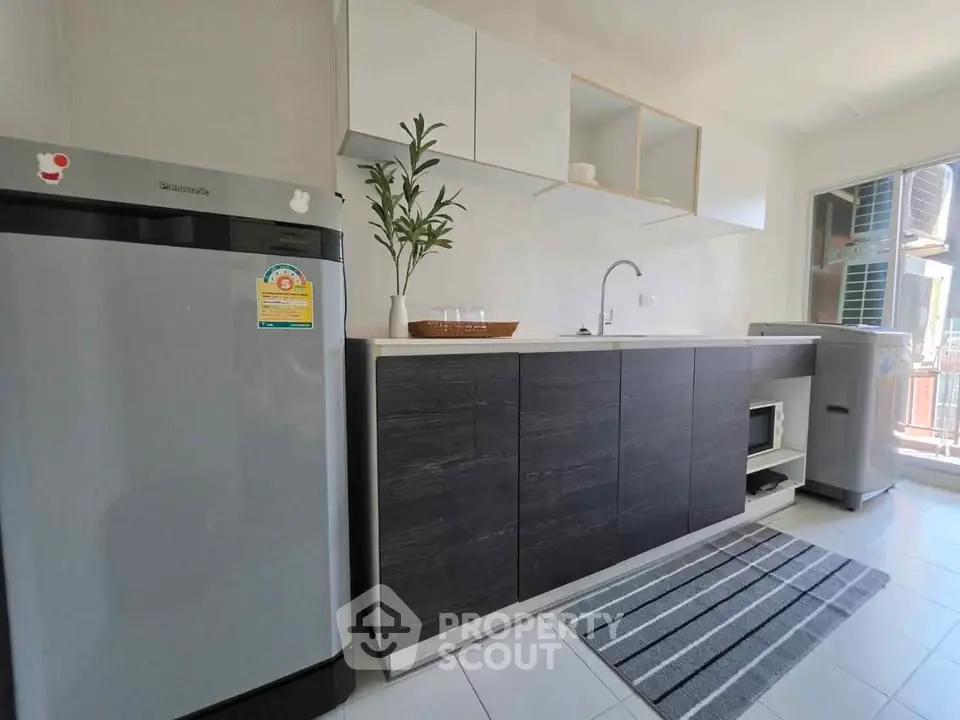Modern kitchen with sleek cabinets, fridge, and washing machine in a bright apartment.
