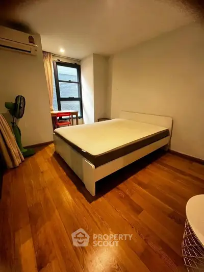Spacious bedroom with wooden flooring and large window in modern apartment