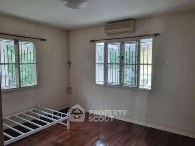 Spacious unfurnished bedroom with wooden flooring and large windows in a serene residential area.