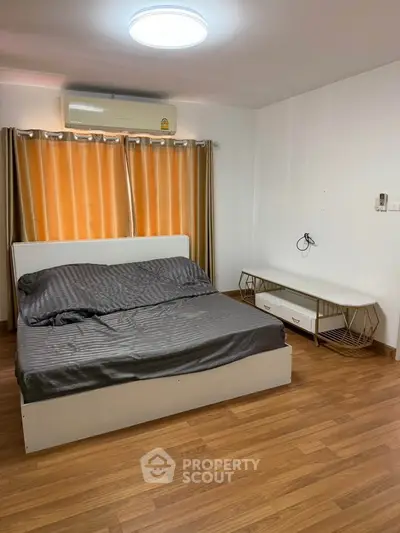 Spacious bedroom with modern furnishings and wooden flooring, featuring a comfortable bed and stylish curtains.