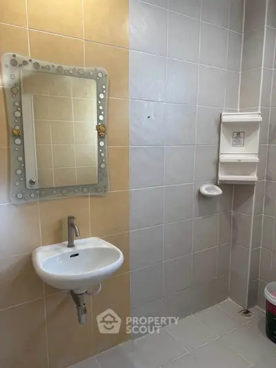 Modern bathroom with stylish mirror and compact sink in a tiled setting.