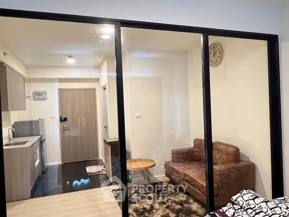 Modern apartment interior with glass partition, cozy living area, and compact kitchen.